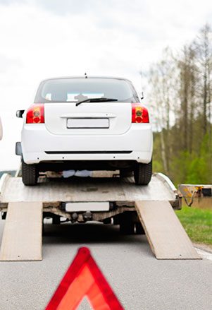 A white car is being towed by a tow truck.