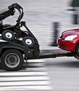 A tow truck towing a red car on the street.