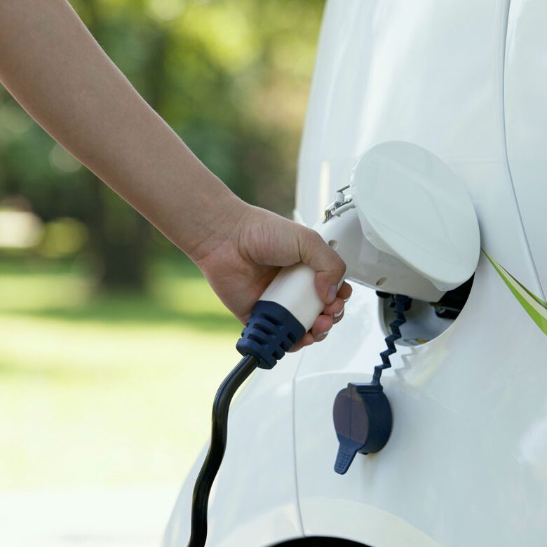 A person charging an electric car in the park.