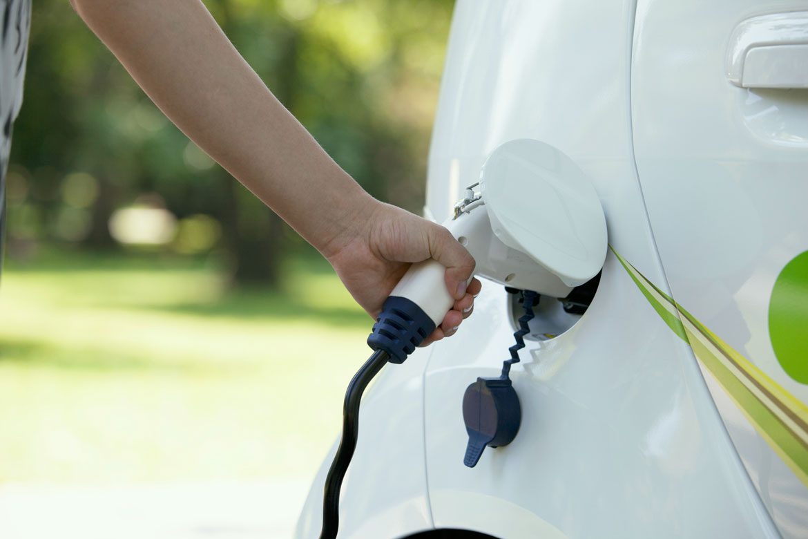 A person charging an electric car in the park.